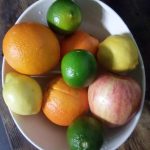 A bowl of fresh fruit including oranges, limes and apples
