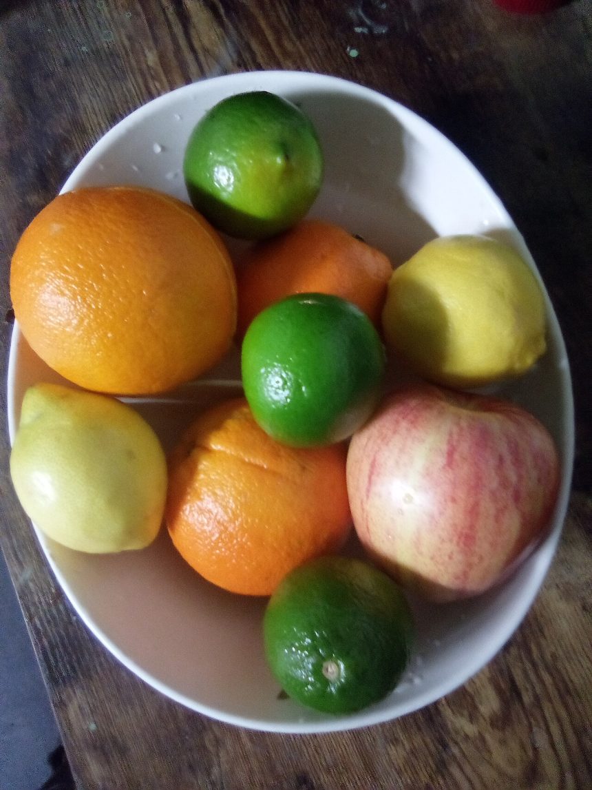 A bowl of fresh fruit including oranges, limes and apples